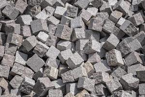 Pile of natural stone cubes for making outdoor pavement tiles. Chaotic stack of road tiles. Stone blocks. photo