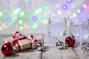 dos copas de champán navideño con cajas de regalo y adornos de bolas contra un fondo claro de bokeh foto