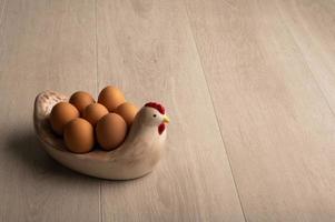 Eggs on a chicken shaped bowl a light wood background and room for copy photo