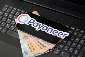 TERNOPIL, UKRAINE - SEPTEMBER 6, 2022 Payoneer paper logotype lies on black laptop with ukrainian hryvnia bills. Payoneer is American financial services company provides online money transfer photo