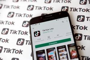 Ternopil, Ukraine - May 8, 2022 Tik Tok smartphone app on screen and Many TikTok logo printed on paper. Tiktok or Douyin is a famous Chinese short-form video hosting service owned by ByteDance