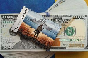 TERNOPIL, UKRAINE - SEPTEMBER 2, 2022 Famous Ukrainian postmark with russian warship and ukrainian soldier as wooden souvenir on big amount of US dollar bills photo