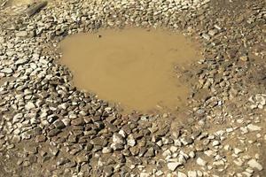 Puddle in road. Pit on rural road. Stones and water. photo