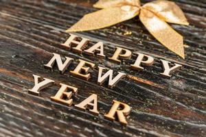 inscripción de feliz año nuevo hecha de letras de madera con lazo dorado. concepto de celebración. fondo festivo foto