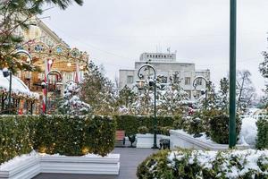 Festive Merry-go-round carousel in winter Square among christmas treees. Magic snowy cityscape. photo