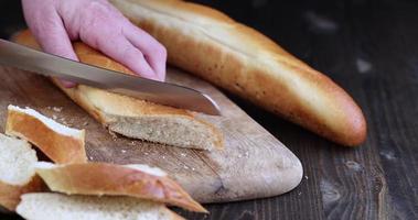 cortar una baguette de trigo en trozos con un cuchillo foto