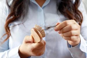 vista trasera mujer joven preocupada por el problema de pérdida de cabello, desequilibrio hormonal, concepto de estrés. muchos cabellos caen después de peinarse con un cepillo de pelo en la mano. mujer desenredó su cabello con un peine, cuidado de la salud foto