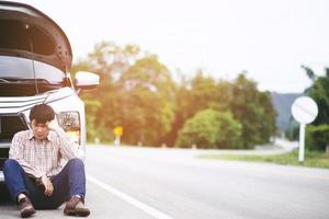 close up businessman hand using a mobile smart phone call a car mechanic ask for help assistance because car broken roadside. people journey friends sit wait beside broken car photo