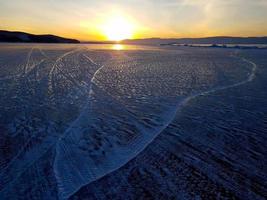 hermosa escena de puesta de sol del lago baikal en invierno, con textura y patrón pintoresco de huellas de neumáticos en la superficie de hielo. foto