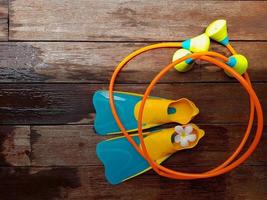 Top view of pair of colorful flippers and toy swimming aid for kid diving practice on wooden background with copy space. photo