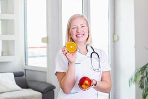 nutricionista sonriente en su oficina, sostiene una fruta y muestra verduras y frutas saludables, salud y concepto de dieta. nutricionista femenina con frutas foto