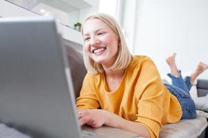 Smiling albino woman working from home, typing email on laptop, sitting on sofa. Surfing web at home. Side view of attractive young woman working on laptop and smiling while sitting on the couch photo