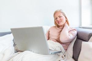 sentirse cansado. mujer joven frustrada que parece exhausta y masajea su cuello mientras trabaja en su computadora portátil desde casa foto