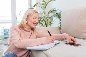 Girl studying the day before the exam, writing notes with a pencil. Pretty young girl doing her studies at home sitting on the floor in the living room with a book reading a binder of class notes photo