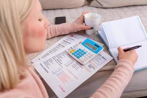 Candid shot of beautiful young Albino woman sitting with calculator and bills, doing paperwork. Hand woman doing finances and calculate on desk about cost at home office.Concept finances and economy photo