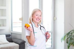 Portrait of beautiful smiling female nutritionist holding an orange. Nutritionist with healthy fruit, juice and measuring tape. Dietitian working on diet plan. photo