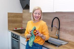 linda chica con cabello rojo rubio azotando su manzana con una toalla de cocina. mujer joven limpiando su fruta en su cocina. ingesta diaria de vitaminas con frutas, dieta y alimentación saludable foto