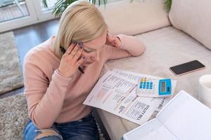 hermosa joven albina sentada con calculadora y facturas, haciendo papeleo. mano mujer haciendo finanzas y calcular en el escritorio sobre el costo en la oficina en casa. concepto de trabajo desde casa foto