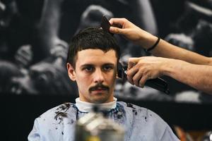 hombre cortándose el pelo a la moda en la peluquería. estilista masculino sirviendo al cliente, haciendo corte de pelo con máquina y peine. foto