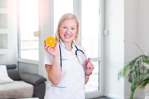 nutricionista sonriente en su oficina, sostiene una fruta naranja y muestra verduras y frutas saludables, salud y concepto de dieta. nutricionista femenina con frutas foto