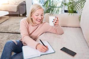 mujer joven que estudia y bebe café, mujer joven estudiosa que trabaja en casa sentada en el suelo en la sala de estar con notas de clase en carpetas estudiando para la universidad foto