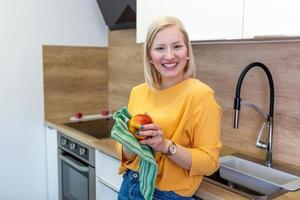 Cute girl with blond red hair whipping her apple with kitchen towel. Young Woman cleaning her fruit in her kitchen. Daily intake of vitamins with fruits, Diet and healthy eating photo