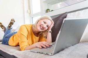 Smiling albino woman working from home, typing email on laptop, sitting on sofa. Surfing web at home. Side view of attractive young woman working on laptop and smiling while sitting on the couch photo
