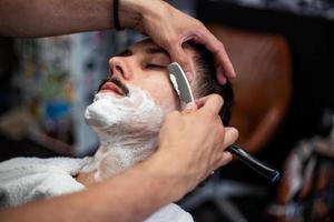 maquinilla de afeitar en manos de peluquero especialista. peluquero afeitando a un hombre en una peluquería, primer plano. hombre con bigotes afeitándose foto