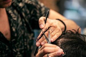 Barbershop. Close-up of man haircut, master does the hair styling in barber shop. Close-up, master Barber does the hairstyle and styling with scissors. Concept Barbershop. photo