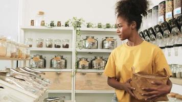 Young African American woman is choosing and shopping for organic products in refill store with reusable bag, zero-waste grocery, and plastic-free, eco environment-friendly, sustainable lifestyles. video