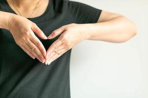 una mujer usa las manos para mostrar el símbolo del amor uniendo las yemas de los dedos para formar un corazón en la parte delantera del pecho izquierdo. foto