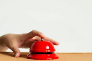 A hand using index finger pressing the bell button of red vintage style handbell on wooden surface in close-up. photo