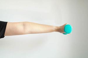 A close-up image of the left hand and arm of a woman lifting dumbbells weighs 1 kilogram in parallel with the floor on a white background. photo