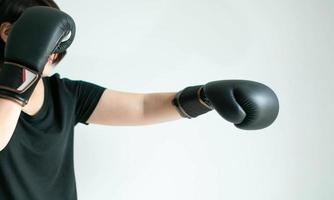 A woman in black boxing gloves stretching her left fist and safeguarding at right. photo