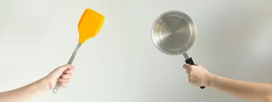 Hands of two people that holding the spade of the frying pan and the pot, the concept of fry and stir fry that has fat versus boil and stewed that is low fat. photo