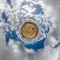 tiny planet in blue sky with beautiful clouds with transformation of spherical panorama 360 degrees. Spherical abstract aerial view. Curvature of space. photo