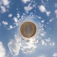 tiny planet in blue sky with beautiful clouds with transformation of spherical panorama 360 degrees. Spherical abstract aerial view. Curvature of space. photo