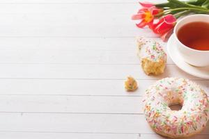 Cup of tea and donuts, flowers tulips on white table with copy space. photo