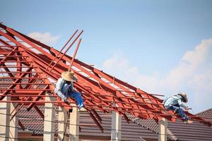 welder workers installing steel frame structure of the house roof at building construction site photo