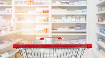 Carro de compras rojo vacío con farmacia farmacia desenfoque de fondo abstracto con medicamentos y productos sanitarios en los estantes foto