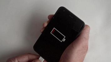 the man holds the charger cable ,another hand holds smartphone ,the smartphone indicator shows the battery charging. video