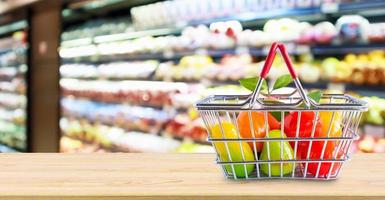 cesta de la compra con fruta en la mesa de madera sobre el fondo borroso del supermercado de la tienda de comestibles foto