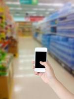 hand holding smartphone with water shelves in supermarket blurred background photo