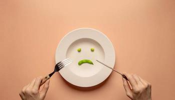 concepto de dieta y cuidado de la salud. tratar de perder peso. mujer joven que usa un tenedor y un cuchillo para comer soja verde en un plato. comida infeliz. vista superior foto