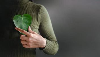 Green Energy, Renewable and Sustainable Resources. Environmental and Ecology Care Concept. Close up of Hand Holding a Heart Shape Green Leaf on Chest photo