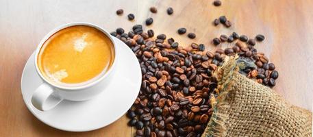 Close-up of a cup of latte with golden foam and mixed or blend coffee beans in a brown sack on an old wooden floor, top view. photo