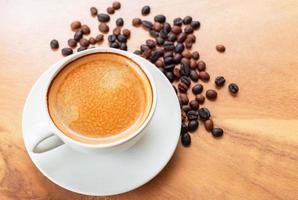 Close-up of a cup of latte with golden foam and mixed or blend coffee beans in a brown sack on an old wooden floor, top view. photo