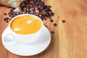 Close-up of a cup of latte with golden foam and mixed or blend coffee beans in a brown sack on an old wooden floor, top view. photo