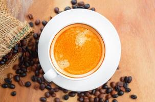 Top view of coffee cup has golden foam and mixed or blend coffee beans in a brown sack on wooden backgrou photo