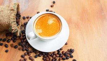 Top view of coffee cup has golden foam and mixed or blend coffee beans in a brown sack on wooden backgrou photo